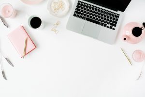 Stock image of a laptop sitting on a white desk with a coffee, pen and notepad