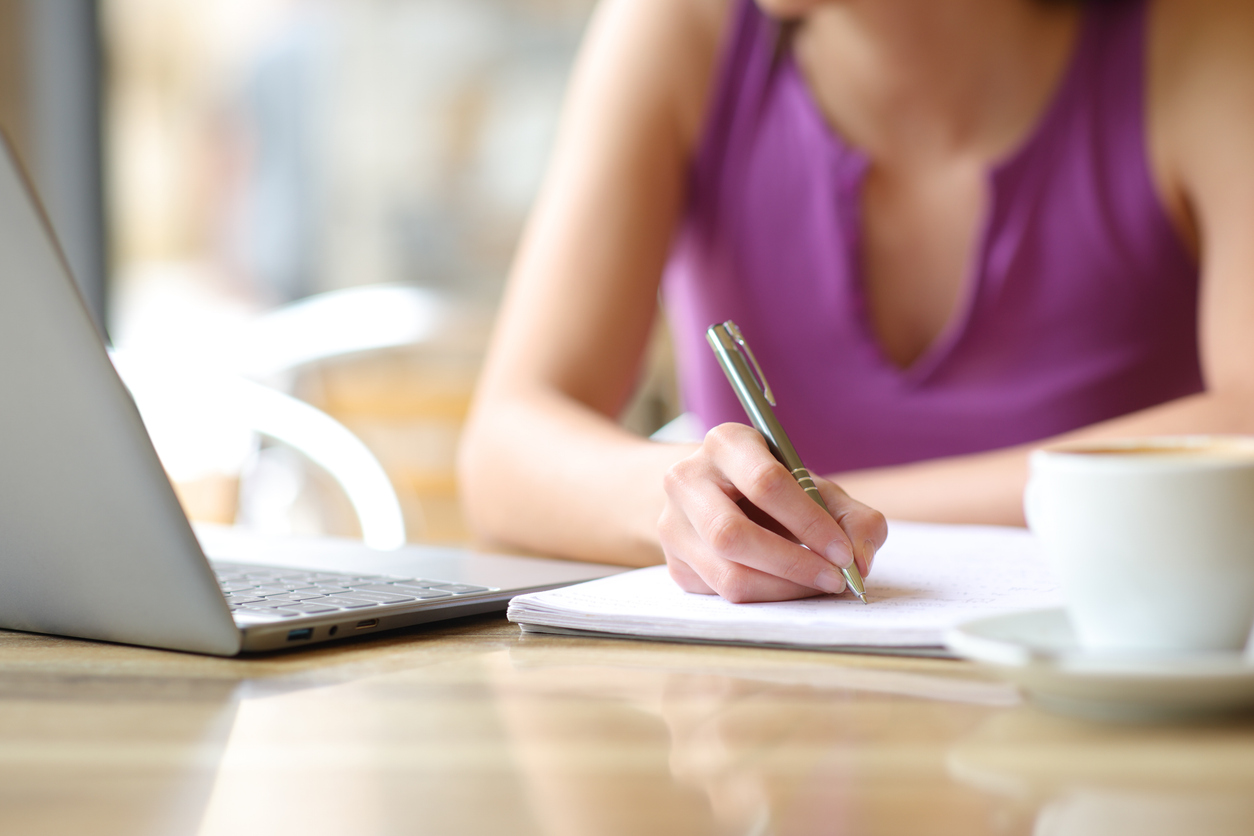 Woman hand writing notes with a laptop and coffee