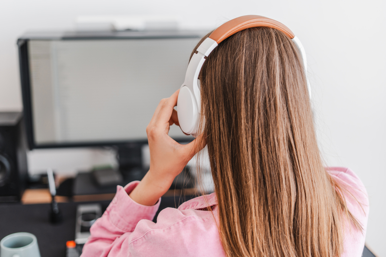 Back view, woman in headphones working in office using computer