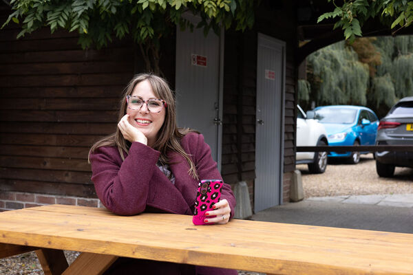 Amy Dawson of Gatekeeper Communications in Ipswich, freelance PR professional sitting at a wooden picnic table outdoors holding a pink phone with black spots