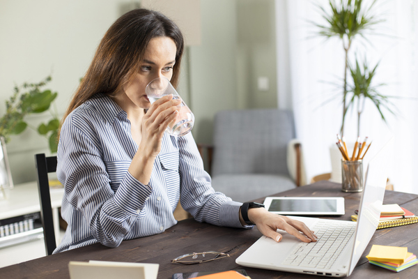 Business owner reviewing research findings and marketing plans while working on a laptop and drinking a glass of water